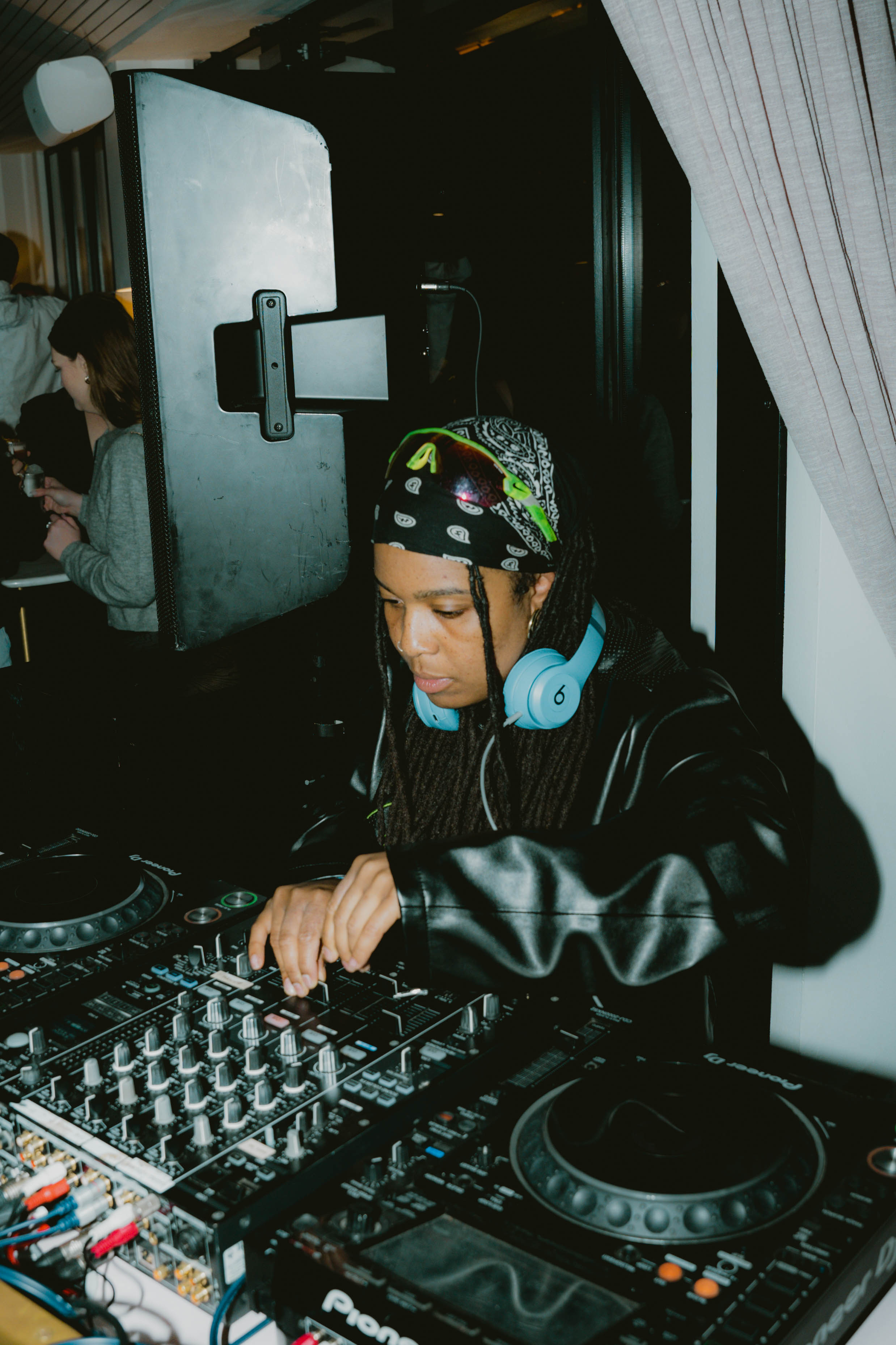 A woman with wearing headphones, skilfully mixing music at a DJ booth creating a lively atmosphere.