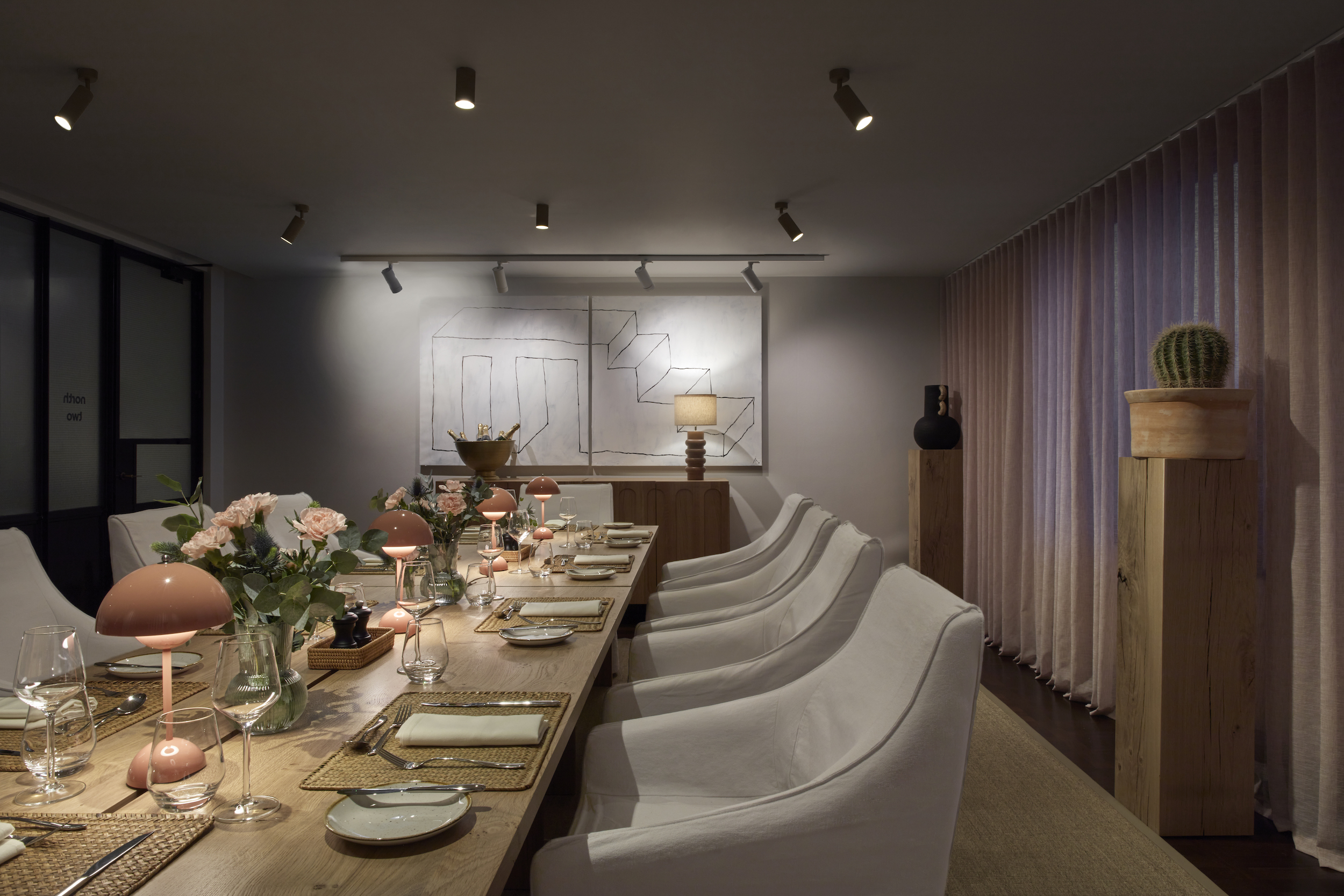 Cosy dining room setup with pink lamps, floral centrepieces, and wall art, creating an inviting atmosphere for guests.