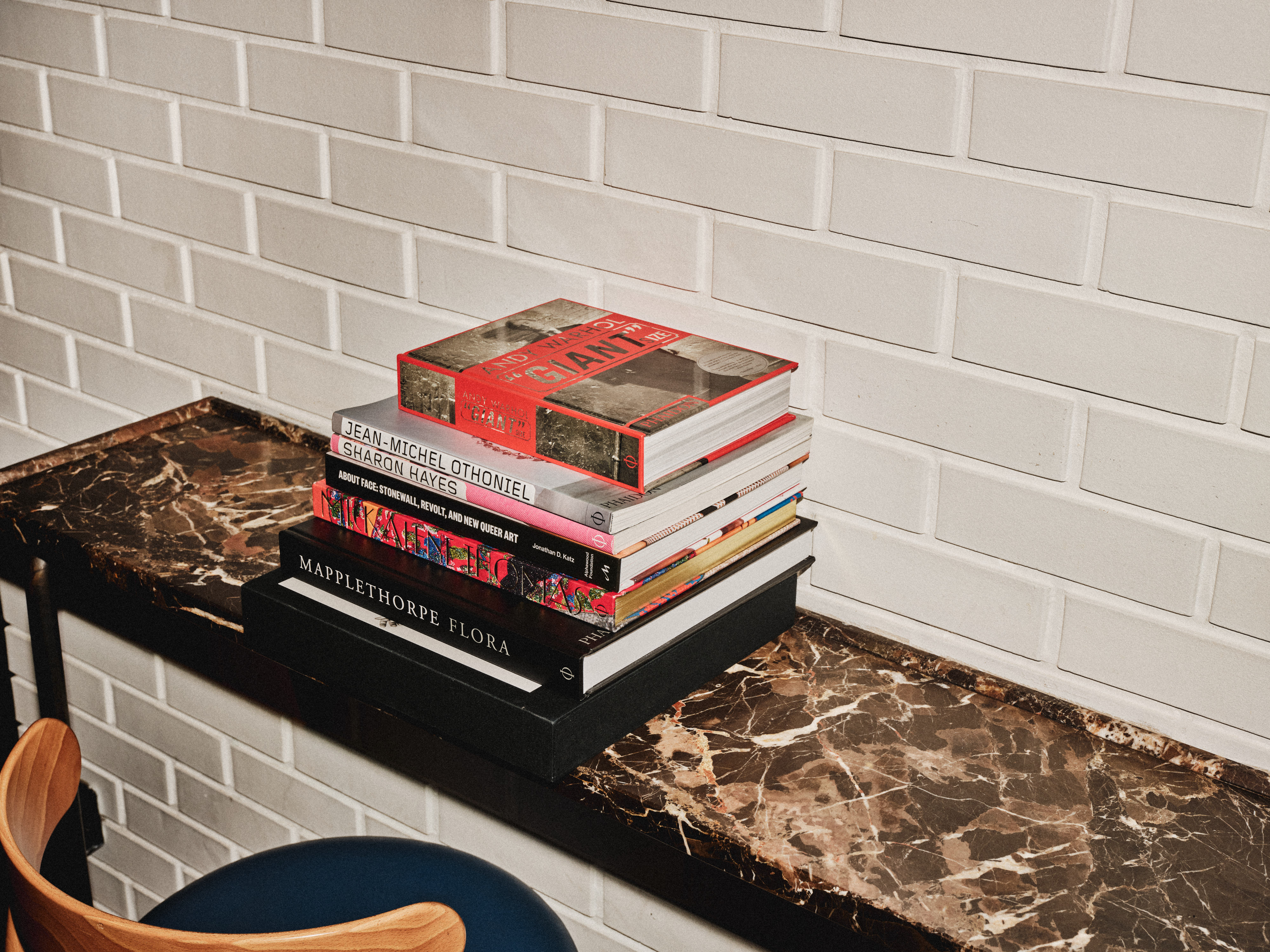 Stack of art books on a marble table against a tiled wall, adding a stylish and intellectual touch to the space.