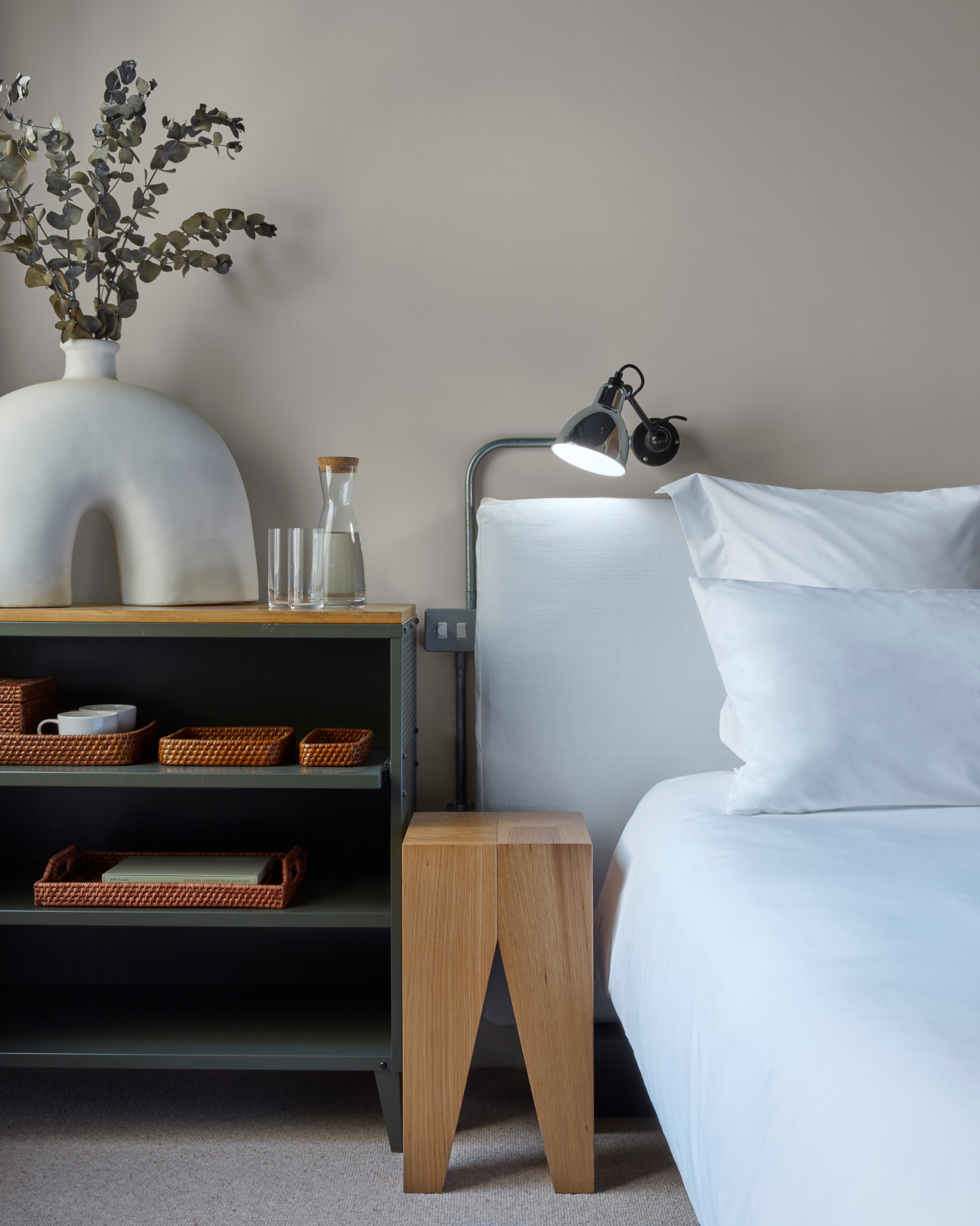 A neatly made bed with white sheets and a decorative vase placed on a table, creating a serene and inviting atmosphere.