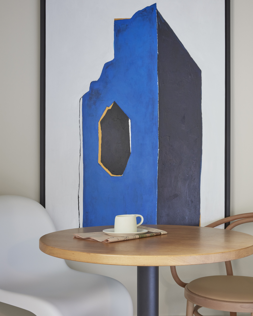 A round table with two chairs positioned beside a colourful painting on the wall.