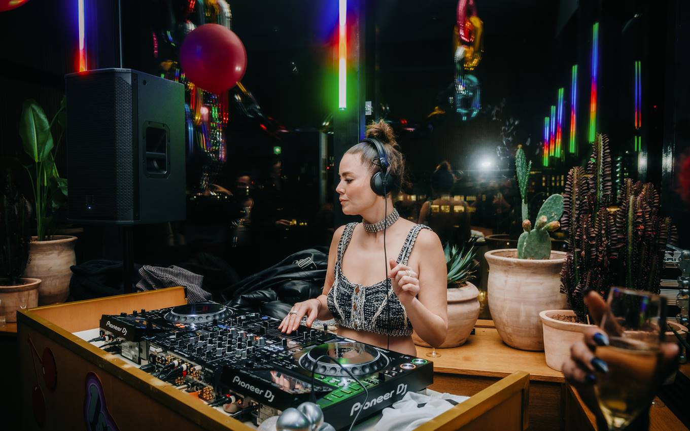 A DJ playing on a mixer, surrounded by neon lights and balloons, creating an upbeat atmosphere for a London party.