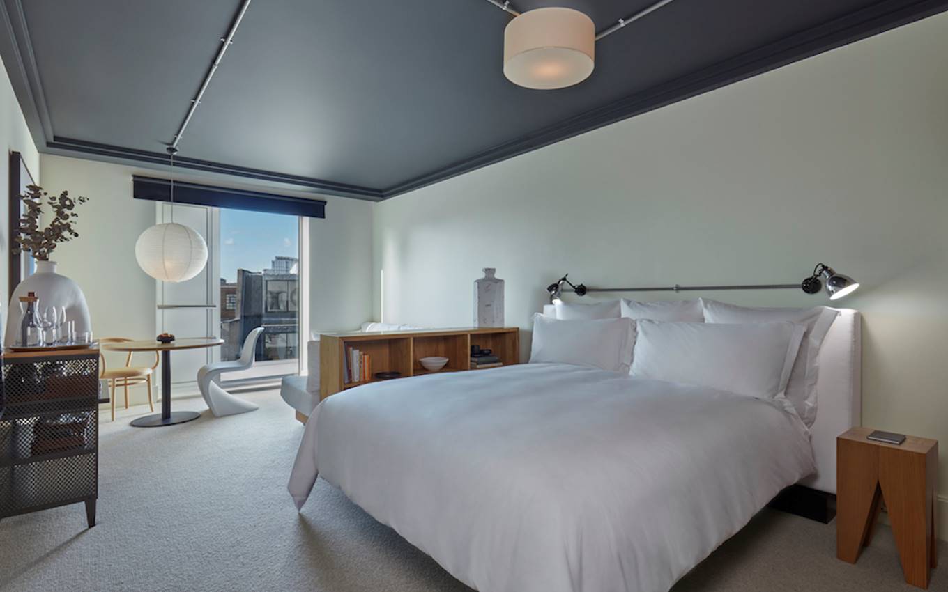 A serene bedroom with a neatly made bed, a functional desk, and a window providing a view outside.