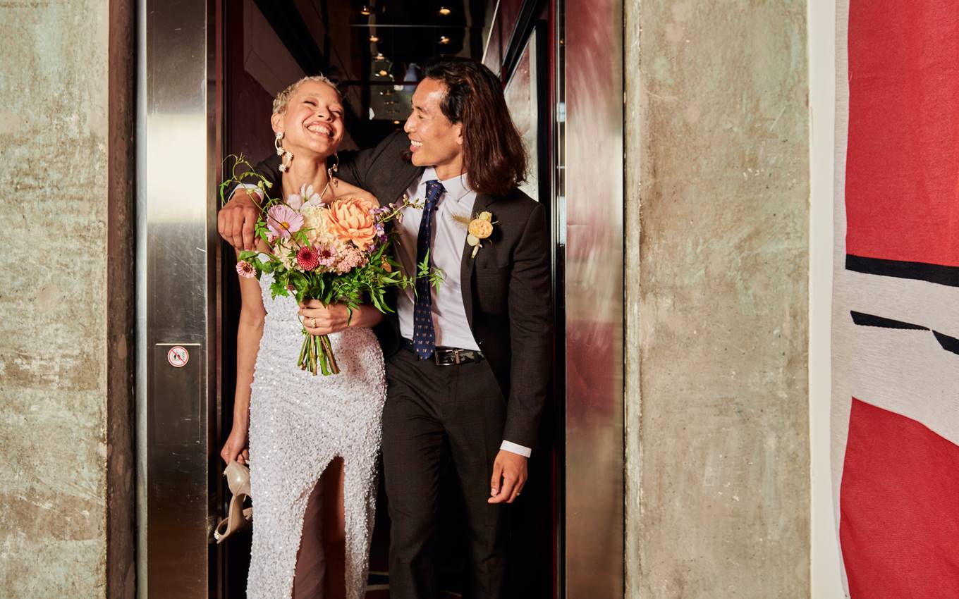 A bride and groom smile together for a photo inside a stylish elevator, capturing a moment of joy on their wedding day.