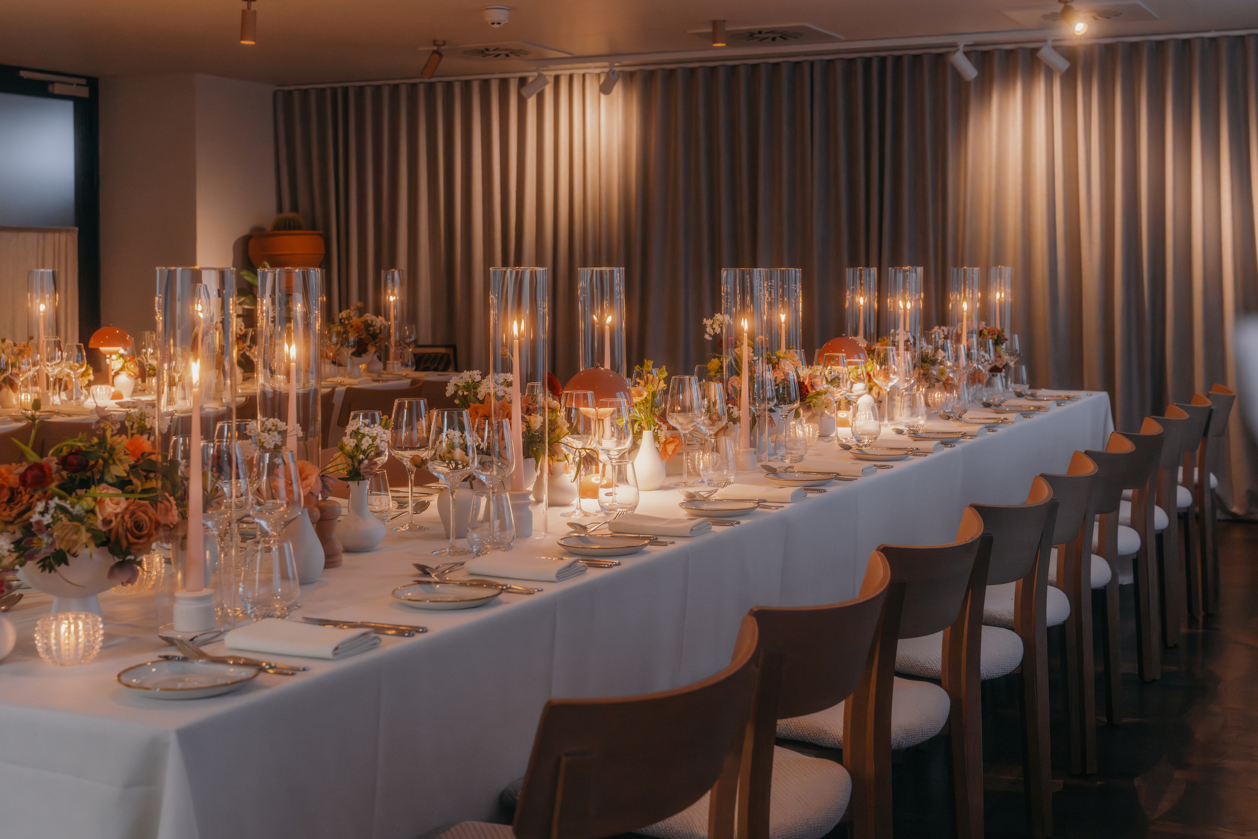 A long table elegantly set with white linens and flickering candles, creating a warm and inviting atmosphere.