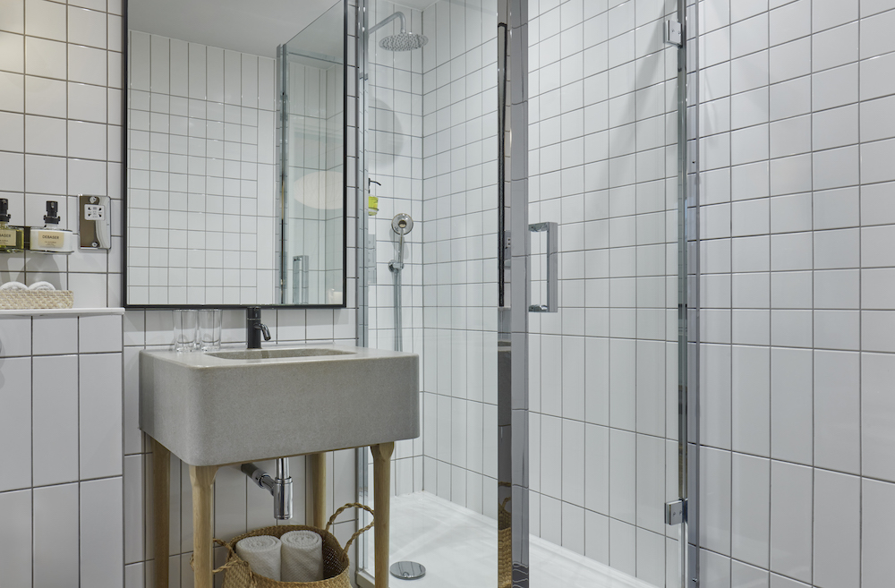Bathroom with white tiles, glass shower door, and wooden accents, creating a clean, modern aesthetic in a London hotel room.