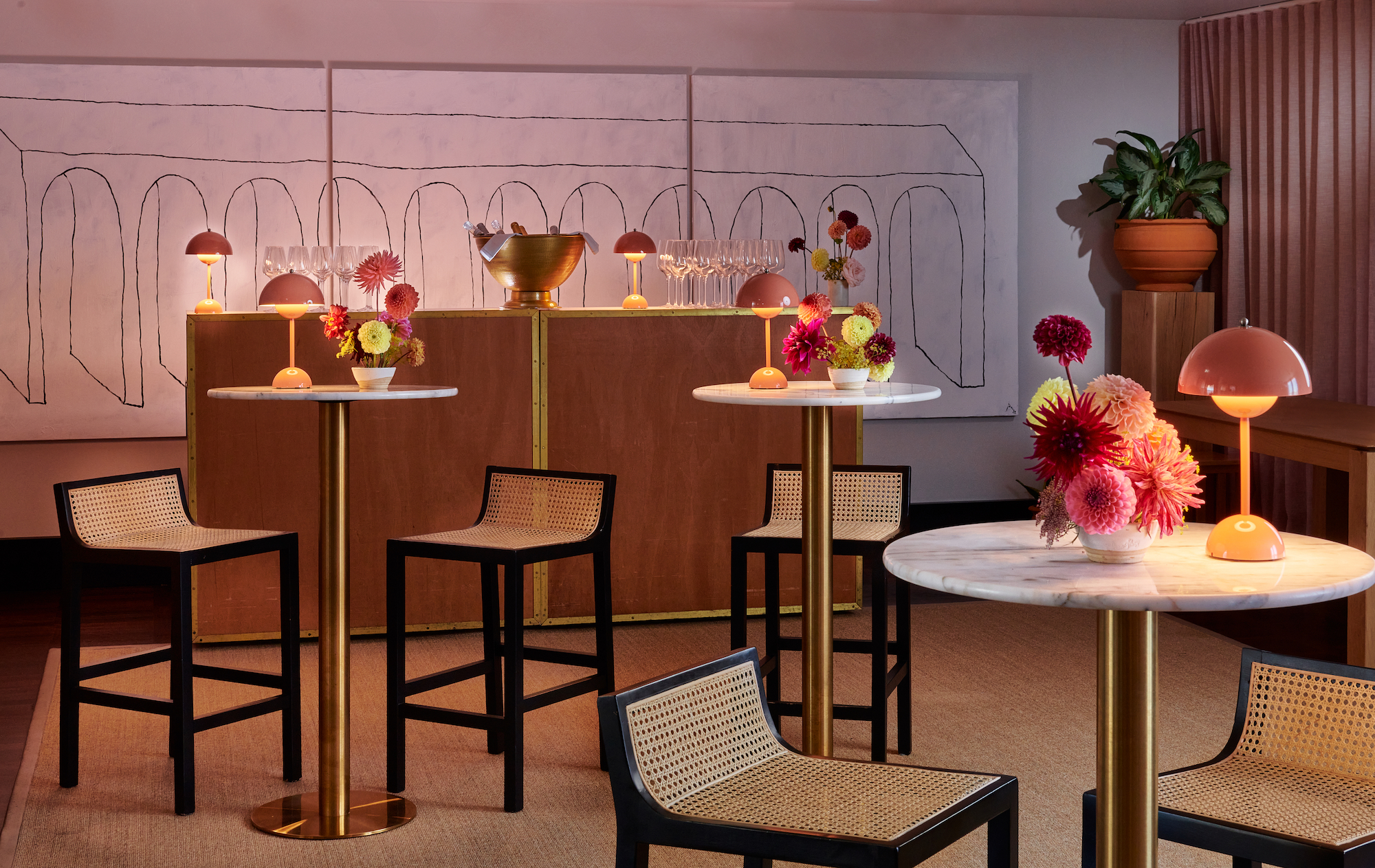 Lounge with black chairs, marble-topped tables, and vibrant red floral arrangements, set against abstract wall art.