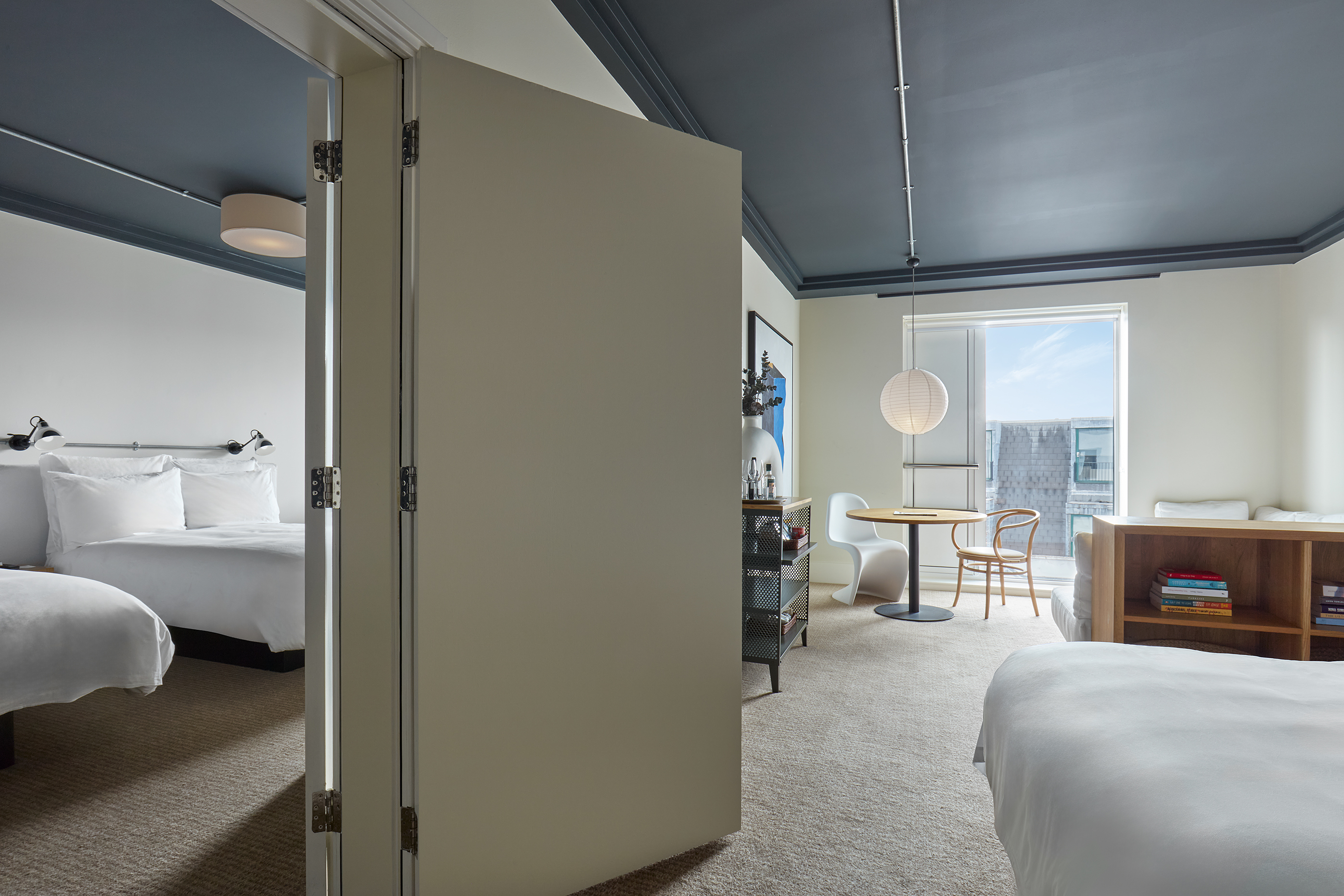 A connected hotel suite in London with two bedrooms, a seating area, and a modern dining space, separated by folding doors.