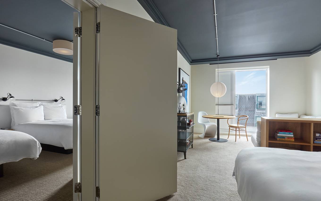 A connected hotel suite in London with two bedrooms, a seating area, and a modern dining space, separated by folding doors.