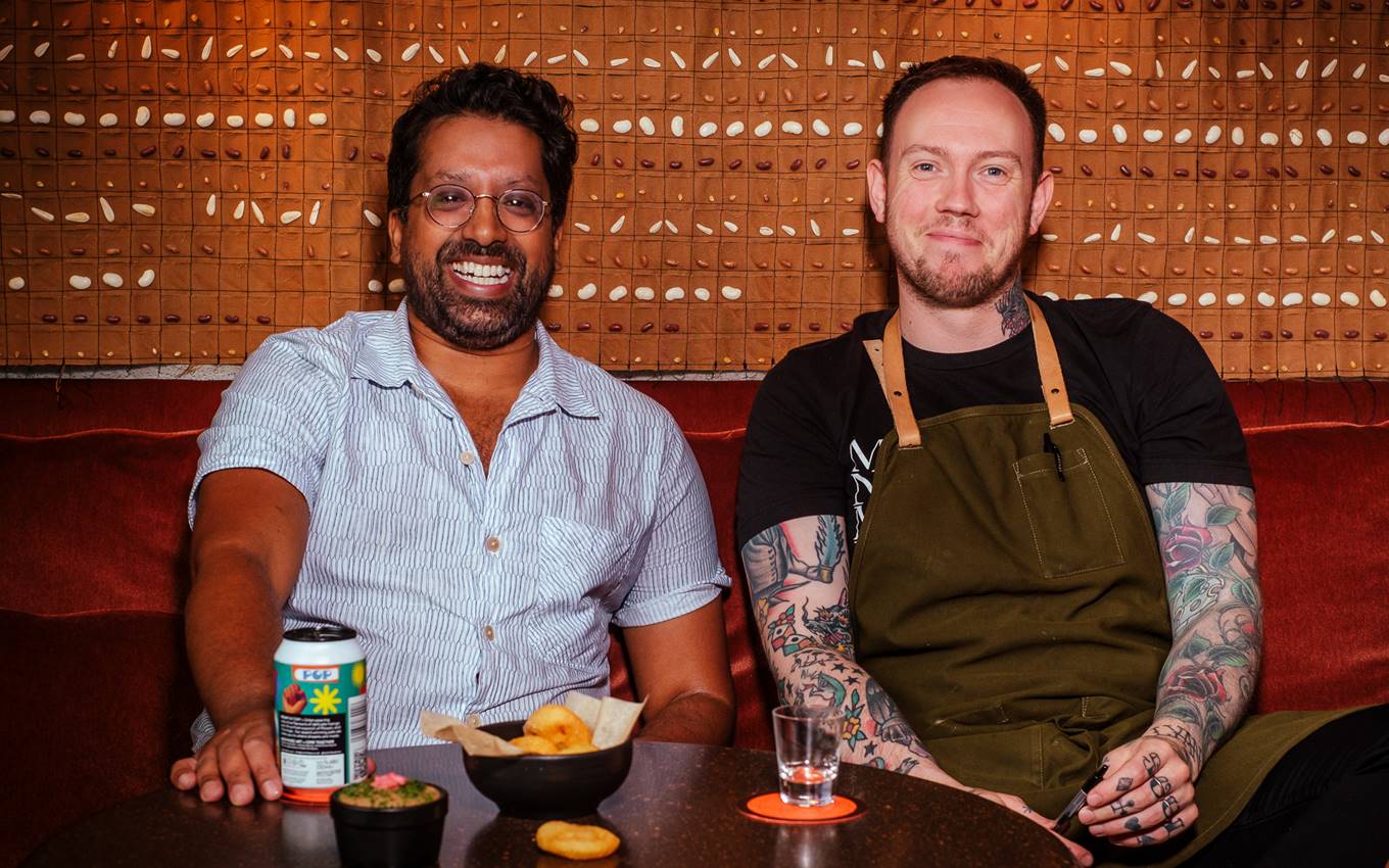 Mr Lyan and Alex smiling while seated at the Seed Library bar in London with drinks and snacks in a warmly lit setting.