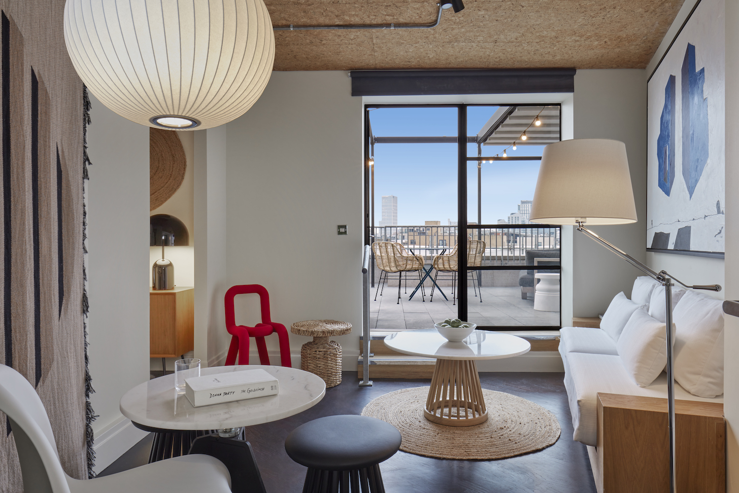 A contemporary hotel suite in London with a mix of modern and rattan furniture, leading to a private balcony with city views.