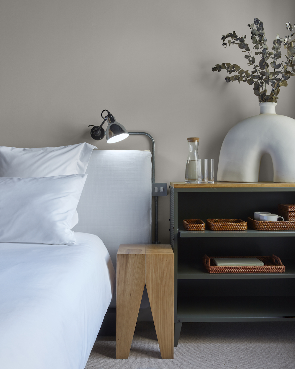 A neatly made bed with white sheets and a decorative vase placed on a night stand, creating a serene and inviting atmosphere.