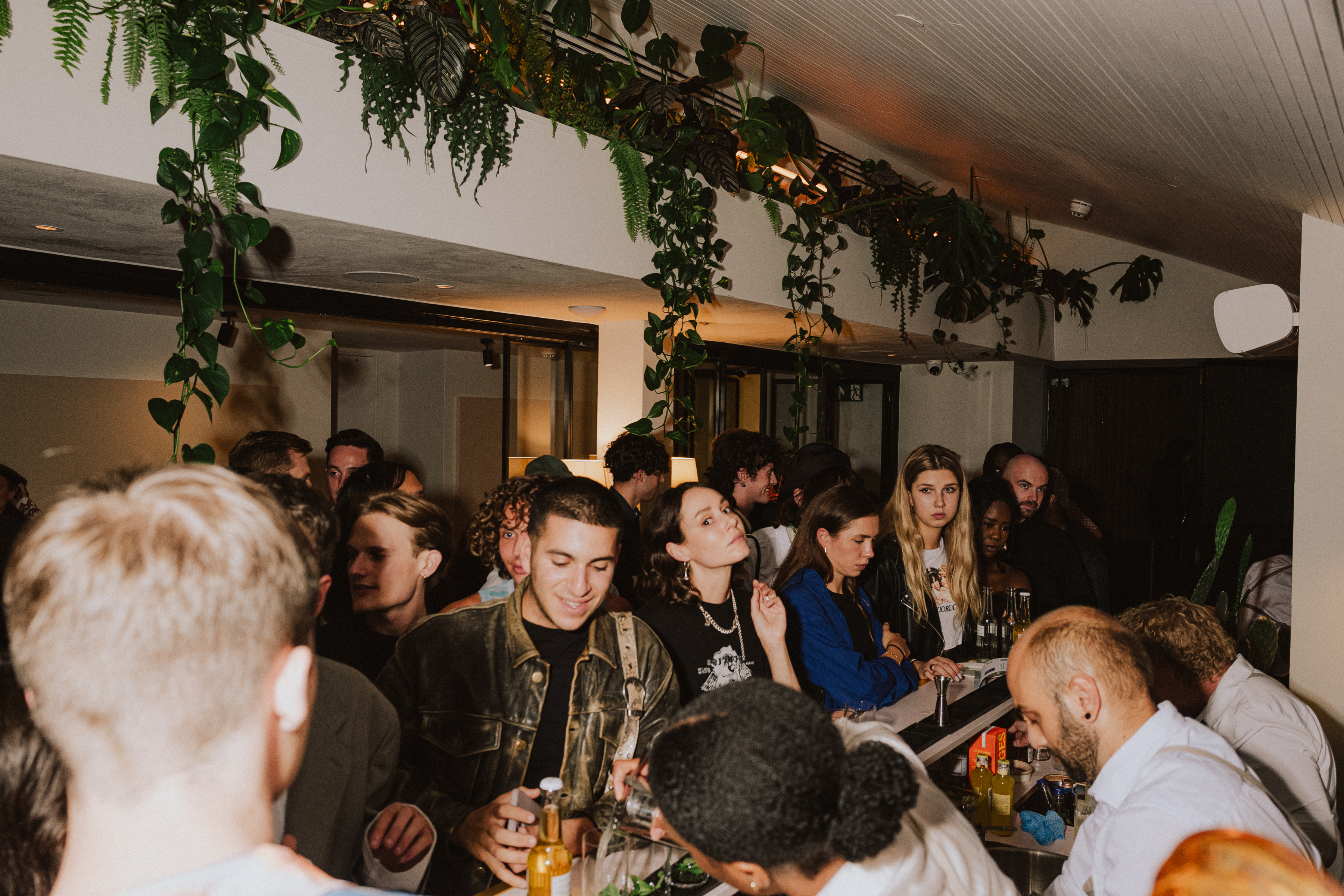 Crowd enjoying a lively London event indoor with greenery hanging from the ceiling, adding a natural element to the ambiance.