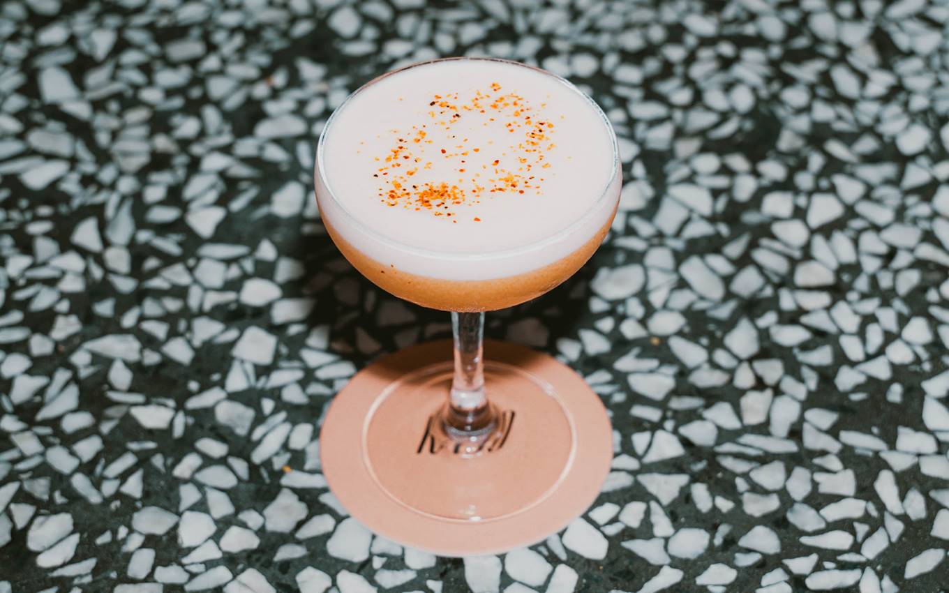 A frothy cocktail in a coupe glass, topped with a sprinkle of spice, sits on a terrazzo bar counter at Kaso.