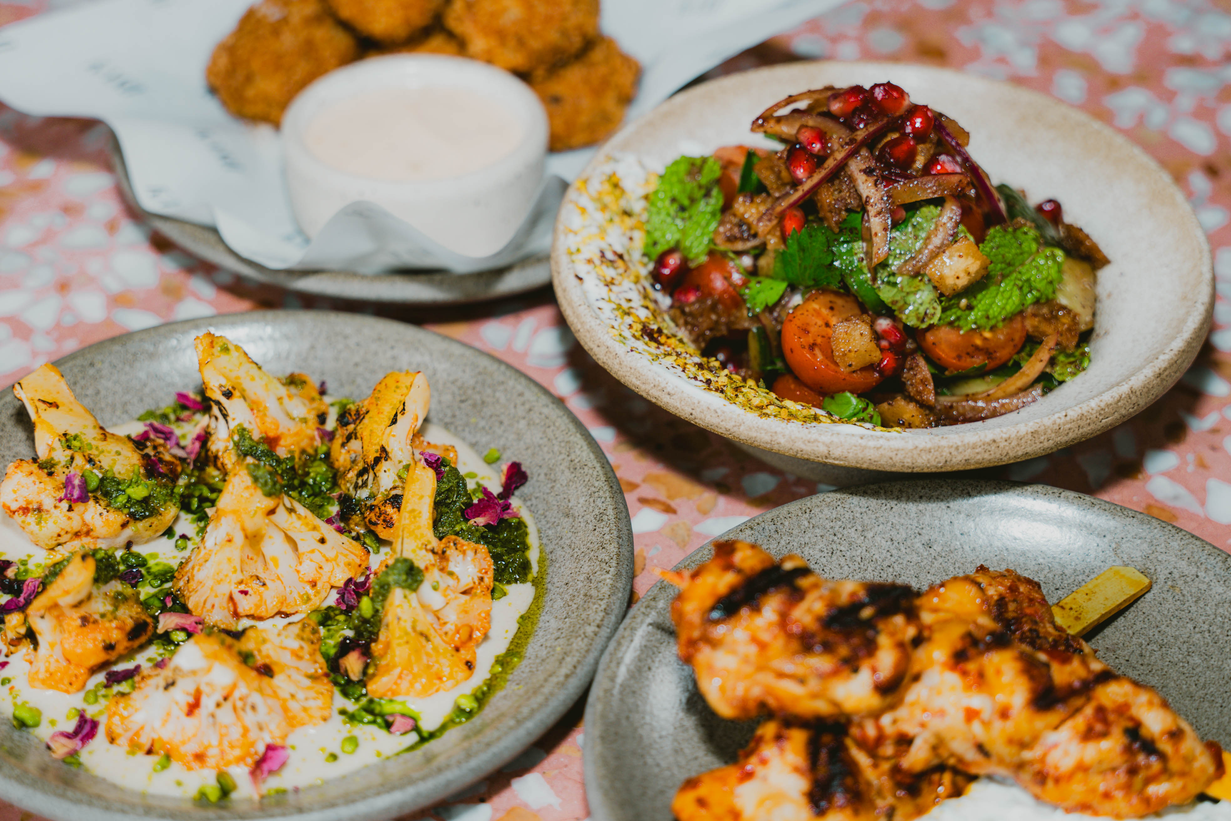 Vibrant Middle Eastern-inspired plates, including grilled cauliflower, salad with pomegranate, and skewered chicken.