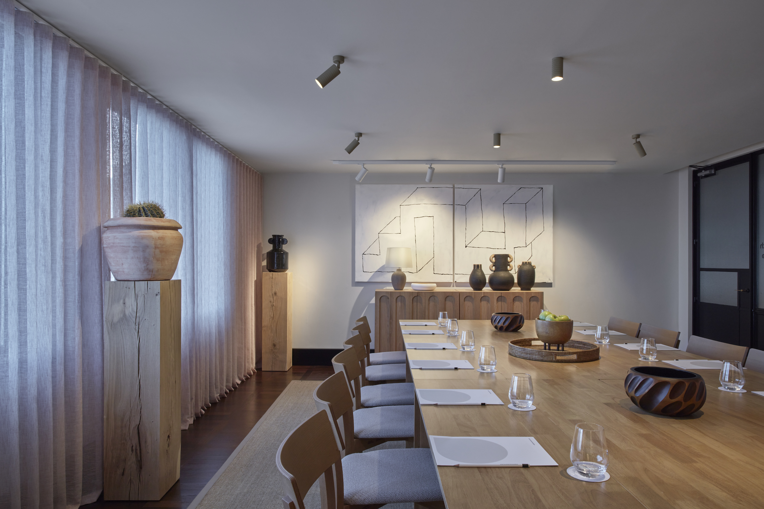 A long table surrounded by chairs, with a painting elegantly displayed on the wall behind it.