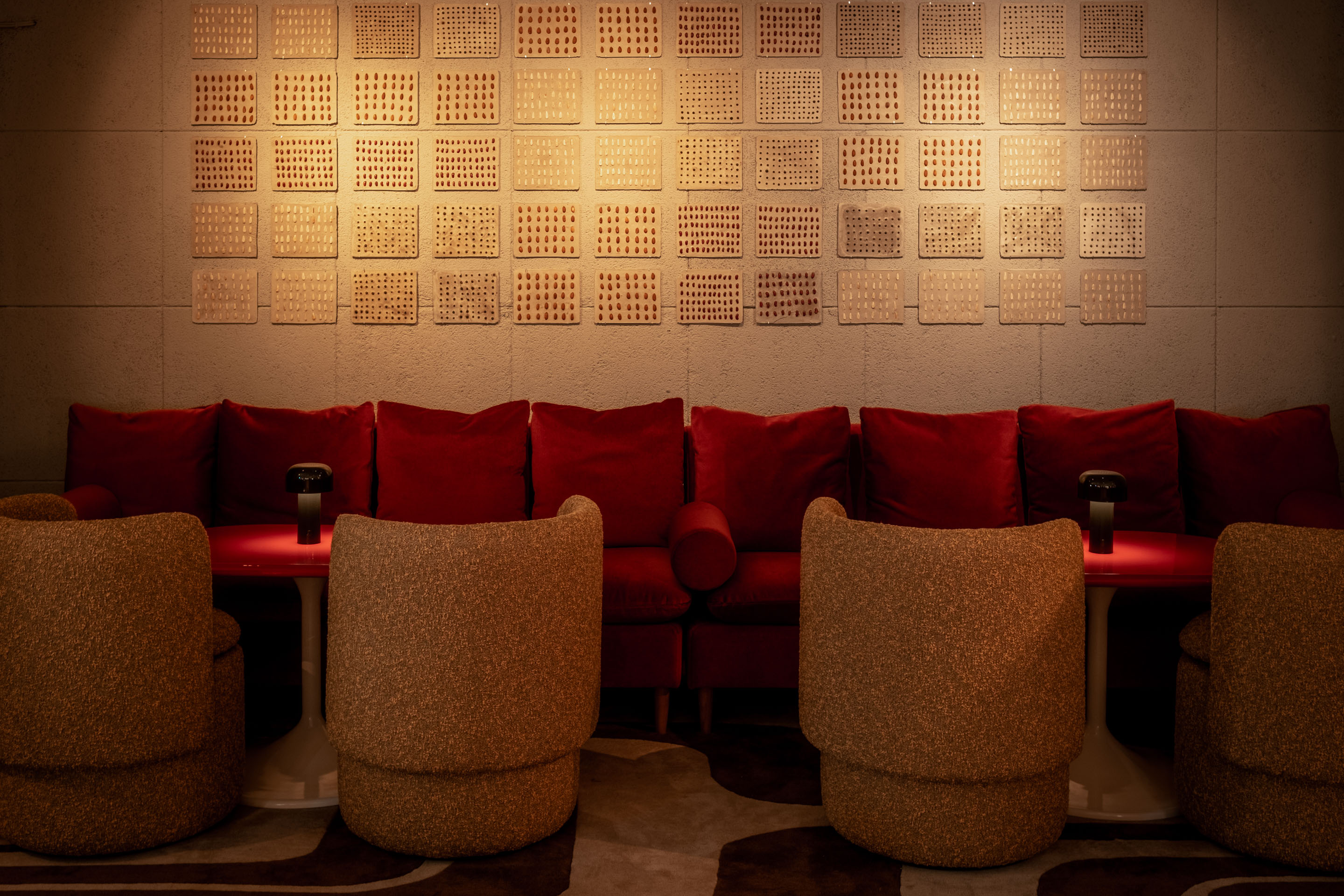Lounge area with red sofa, cosy chairs, and textured wall art at the Seed Library cocktail bar in London.