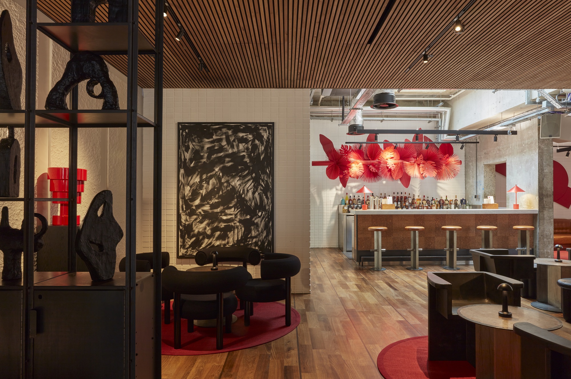 Modern London bar area with wooden floor, red decor accents, and artful lighting featuring abstract black and red wall art.