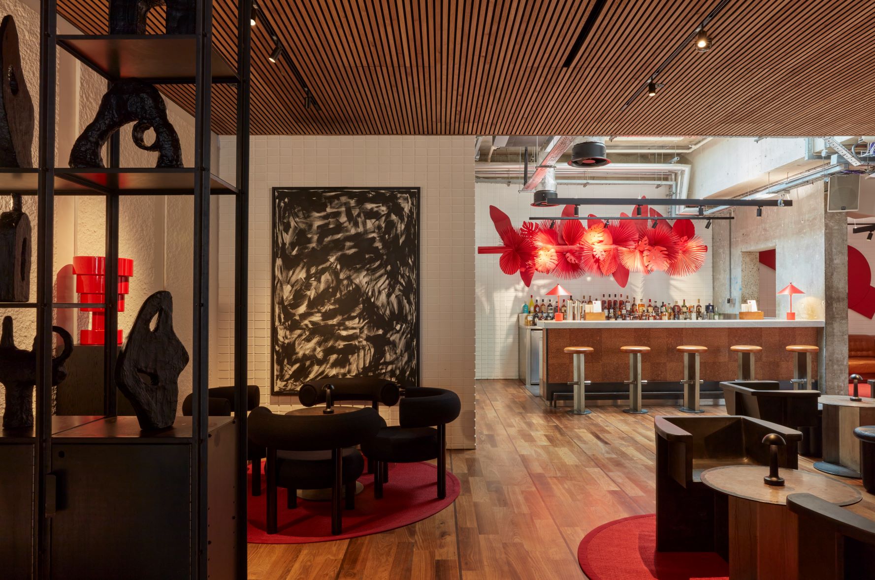 Modern London bar area with wooden floor, red decor accents, and artful lighting featuring abstract black and red wall art.