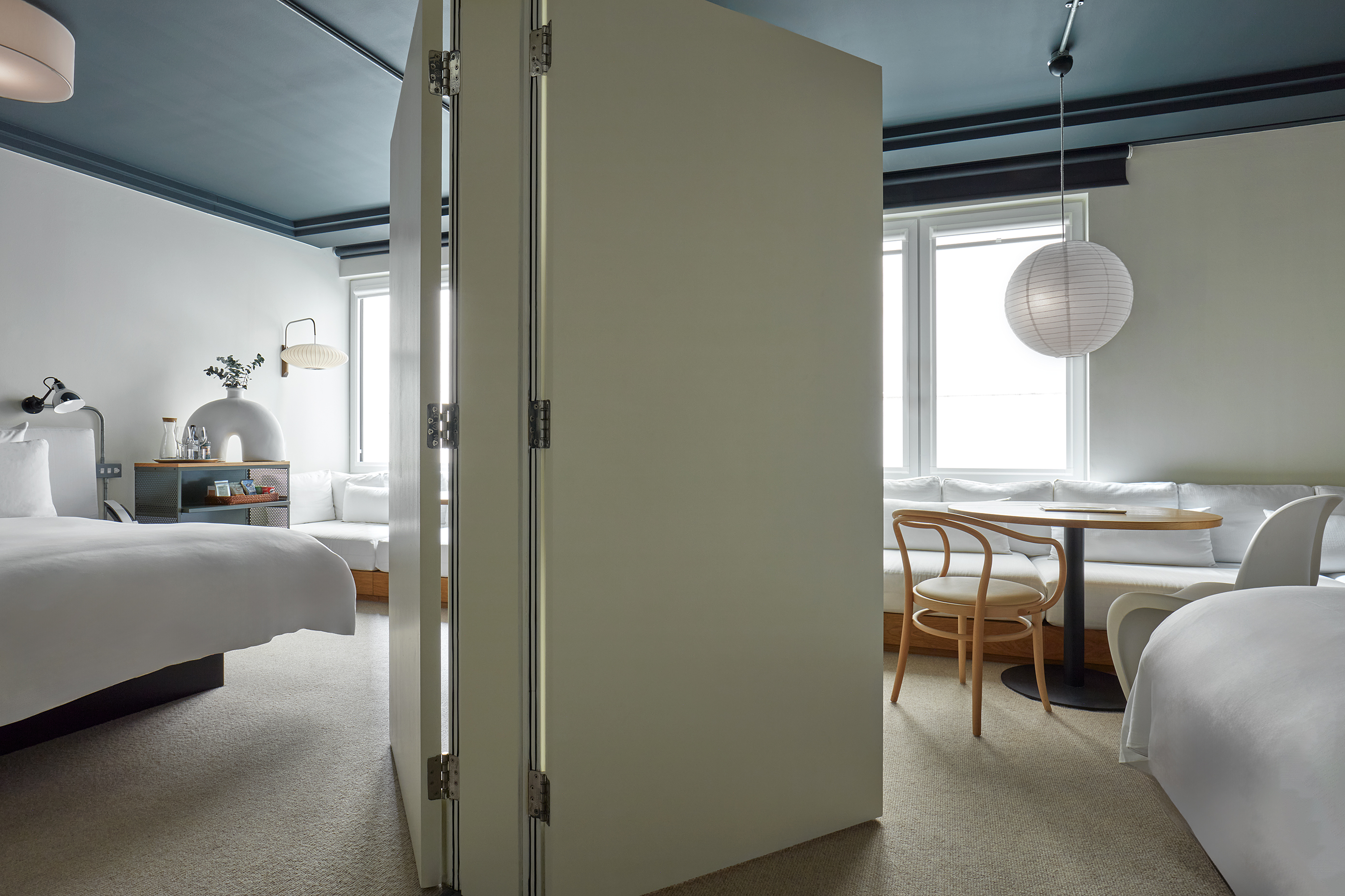 Divided hotel suite at One Hundred Shoreditch with bed, seating area, and round table, separated by a door for privacy.